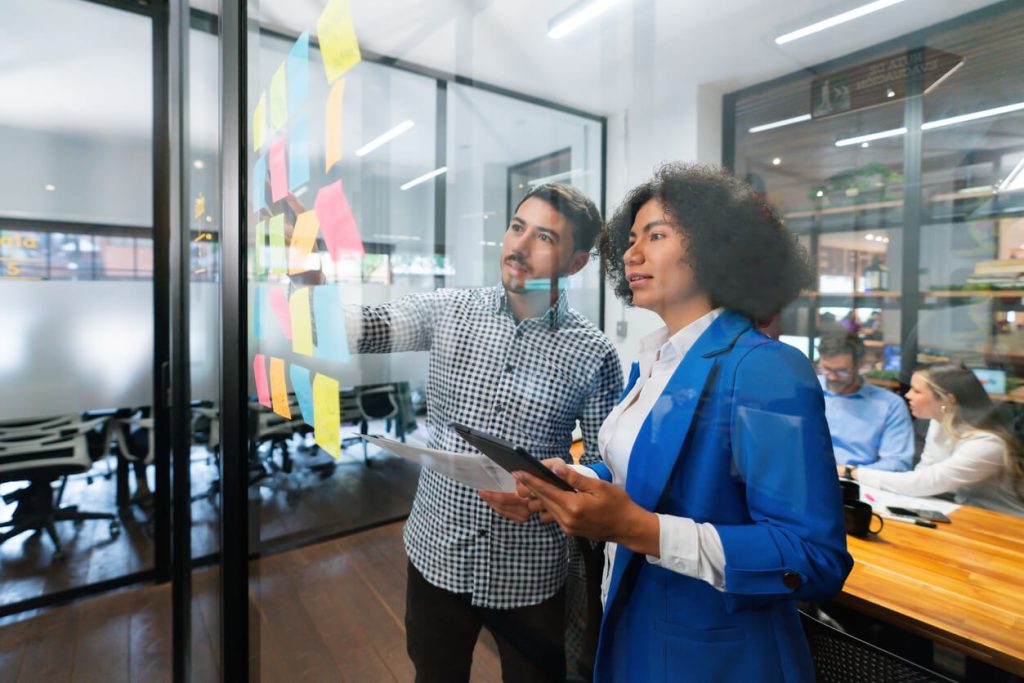 Colegas de trabalhando olhando para post its no vidro