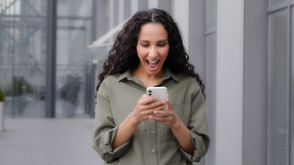 Mulher feliz olhando para o celular e vendo as Recompensas para Campanhas de Incentivo